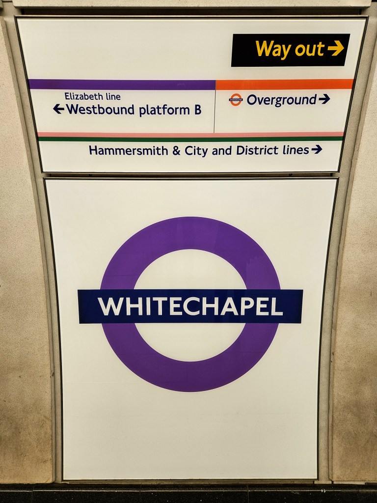 A sign at Whitechapel Station displaying directions for various train lines including the Elizabeth line, Overground, and Hammersmith & City and District lines.