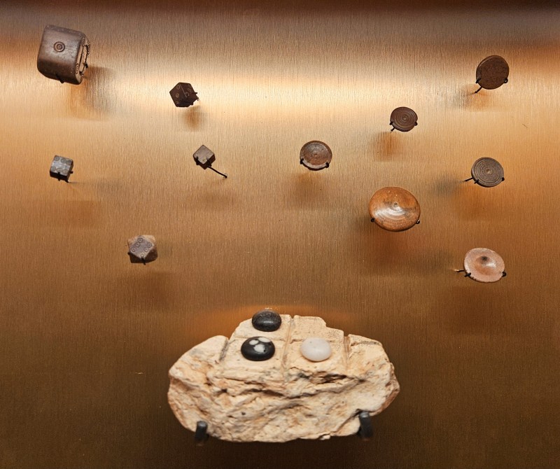 An exhibit display featuring various small historical artifacts attached to a gold background. The items include buttons, stones, and metal pieces, arranged in an artistic manner.