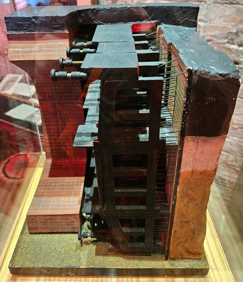 A detailed model of a construction technique used for tunneling, showcasing various components such as support beams and hydraulic systems within a transparent display case.