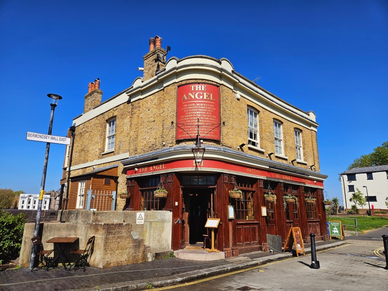 Exterior view of The Angel pub located on Bermondsey Wall East, featuring a traditional brick facade, decorative signage, and a clear blue sky.