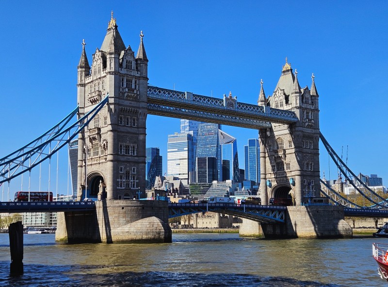 A view of Tower Bridge in London, showcasing its iconic towers and arches against a clear blue sky, with modern skyscrapers in the background.