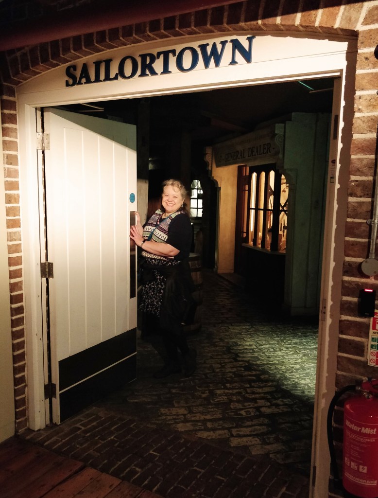 Person standing at the entrance of a building labeled 'SAILORTOWN' in a dimly lit setting with cobblestone flooring.